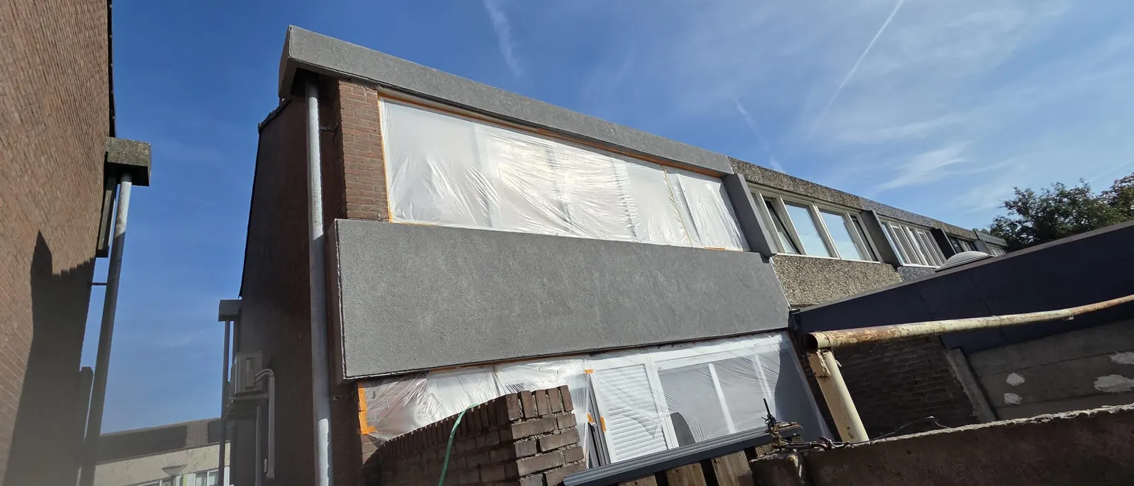 Achtergevel van een woning met afgeplakte kozijnen tijdens een renovatie
