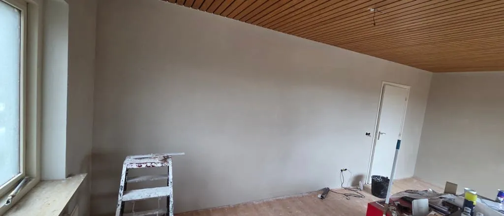 Brede, egaal afgewerkte wand in een woonkamer met houten plafond