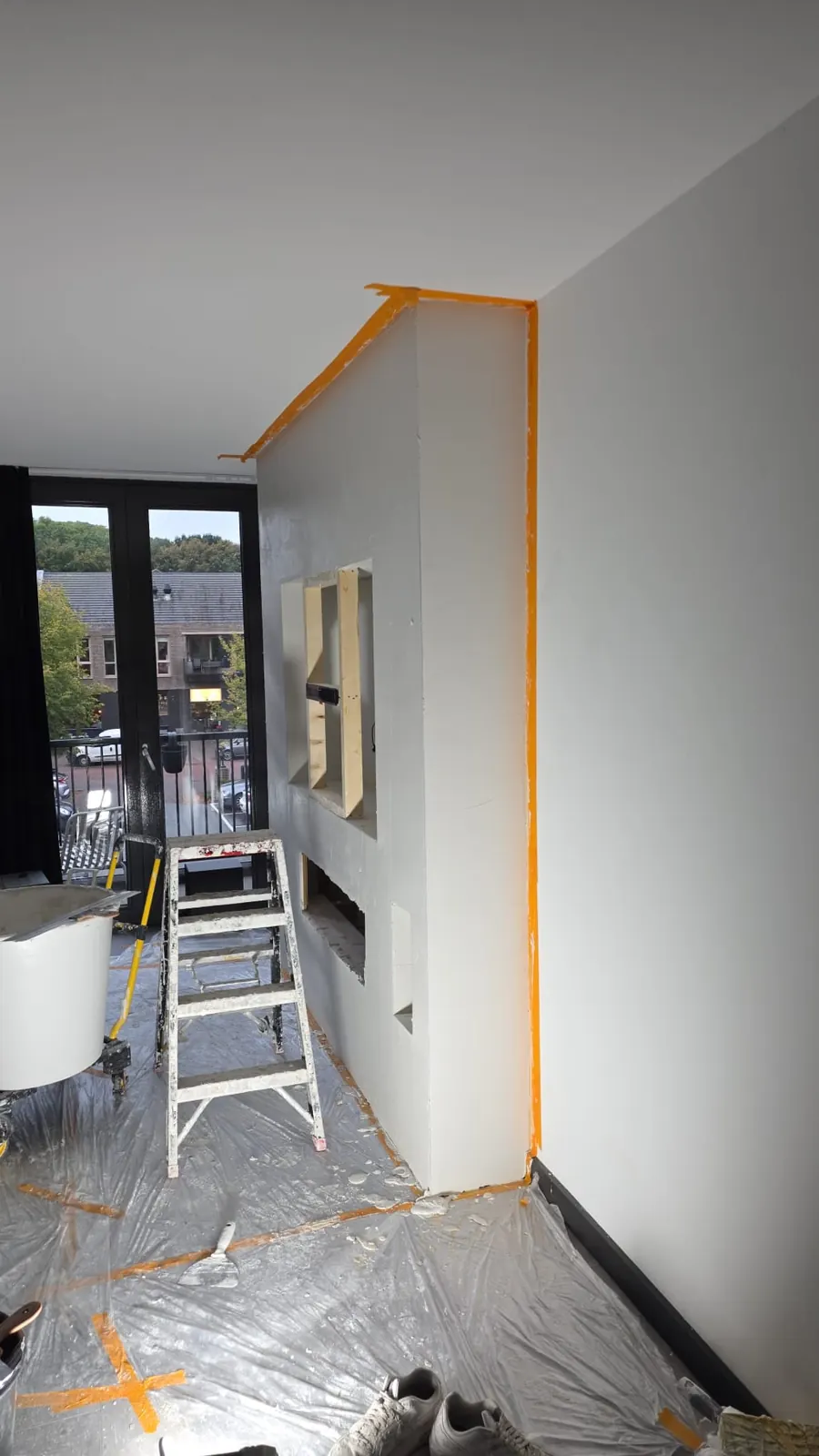 Wand afgeplakt met oranje tape en vloer afgedekt voor het schilderwerk