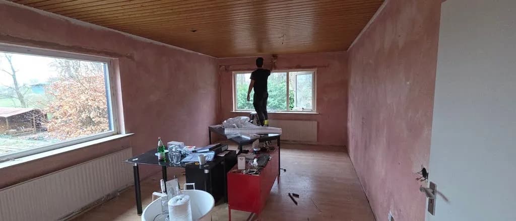 Stukadoor aan het werk bovenin een kamer met vers gestucte wanden